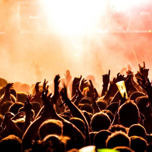 Menschenmenge bei einem Konzert mit erhobenen Händen vor einer hell erleuchteten Bühne